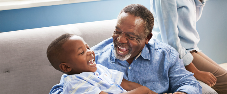 Image of an adult and a child sitting together on a couch laughing (not real patients)
