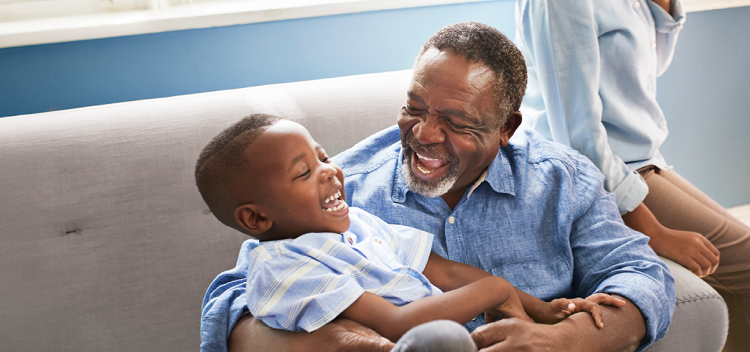 Image of an adult and a child sitting together on a couch laughing (not real patients)