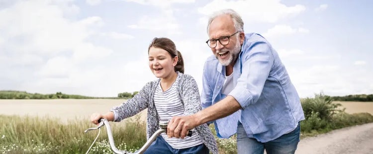 Image of an older man helping a young girl ride a bike (not real patients)