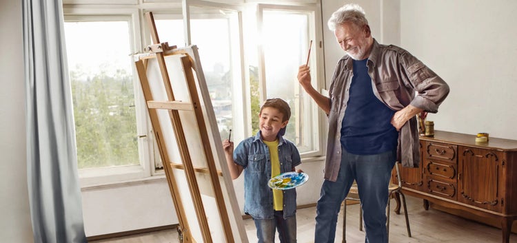 Image of an older man and a boy painting on an easel (not real patients)