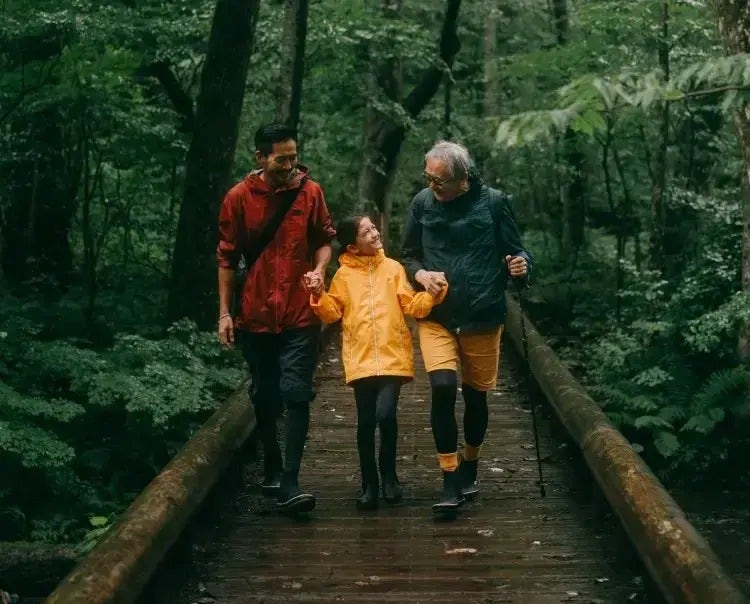 Image of an older man, younger man, and young girl walking on a bridge through a forest (not real patients) mobile