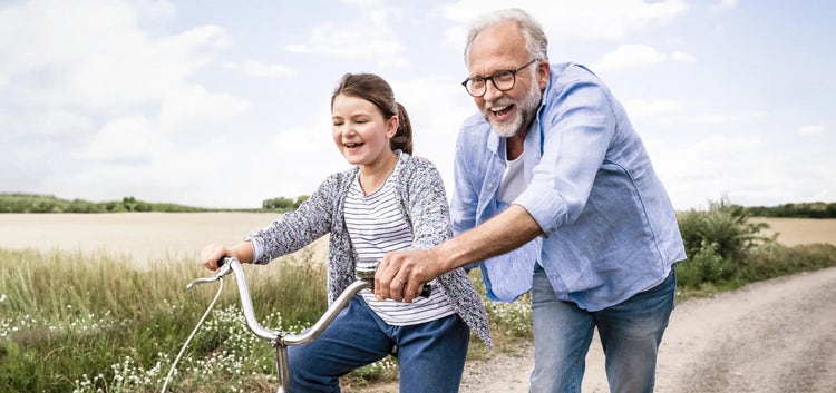 Image of an older man helping a young girl ride a bike (not real patients)