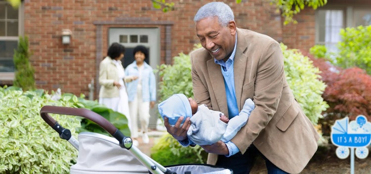 Image of a grandfather placing a baby in a carriage, as a grandmother and mother talk in the background (not real patients)