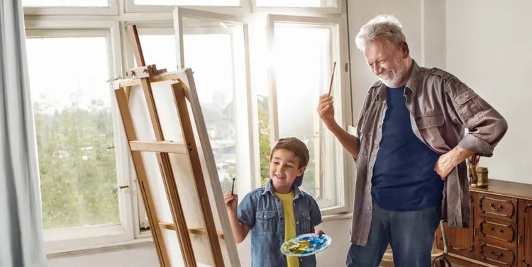Image of an older man and a boy painting on an easel (not real patients)